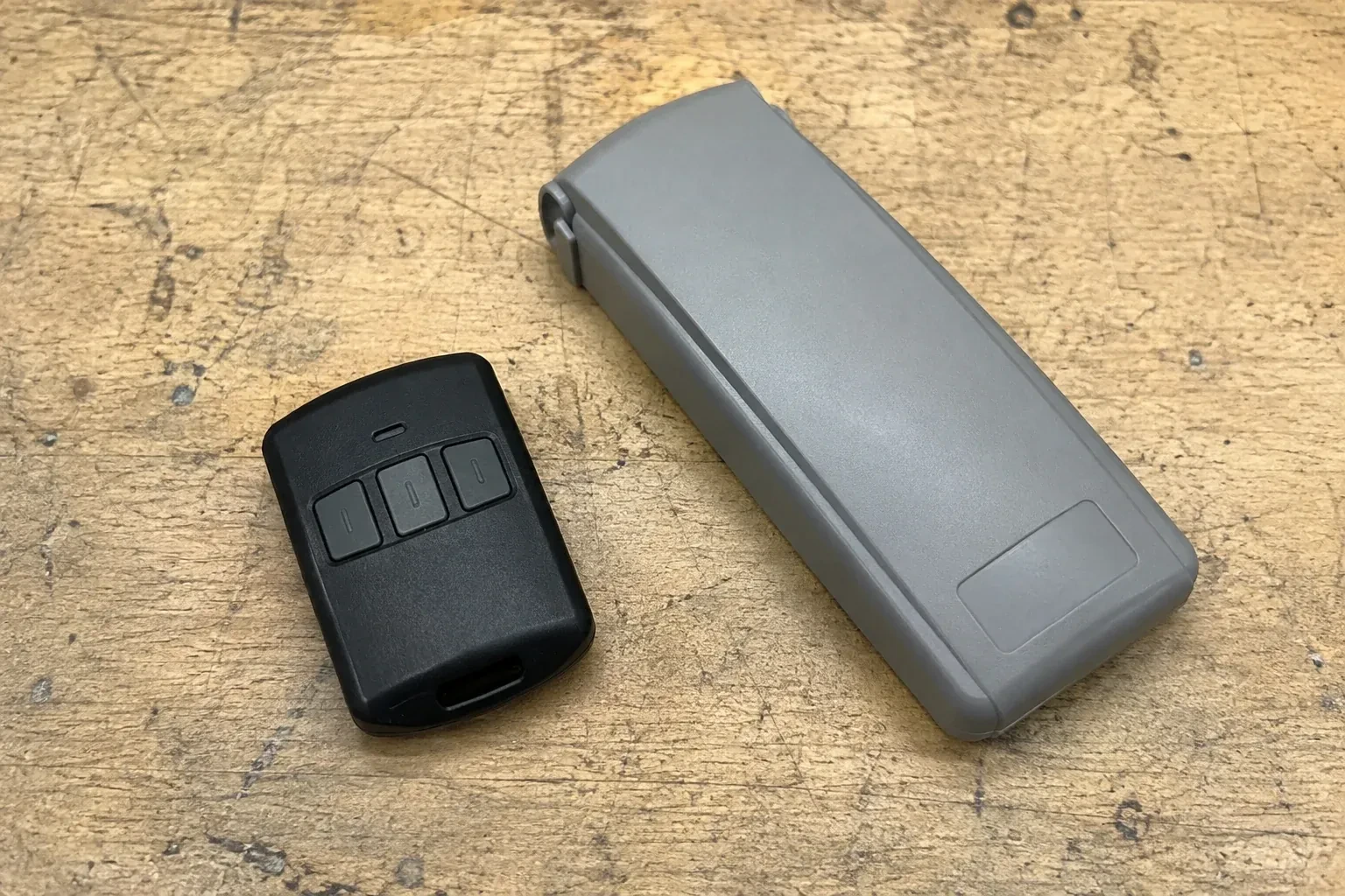 Three-button remote beside a closed grey keypad cover on a workbench. — Garage Door Remote and Keypad Programming, Markham