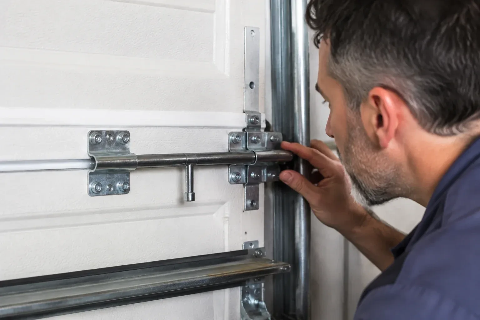 Person leaning close to a white paneled door, one hand on a metal slide-bolt bar mounted across the panel. — Garage Door Manual Lock Repair, Markham