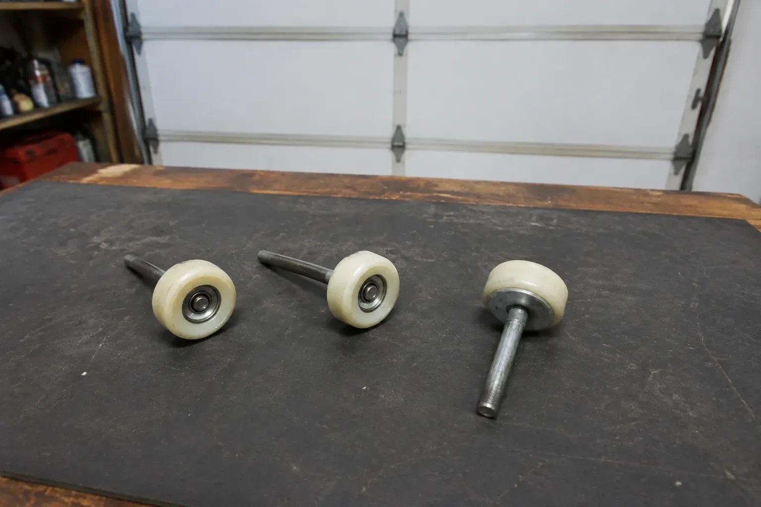 Three detached nylon-wheel garage door rollers with steel stems on a work mat. — Garage Door Roller Replacement, Markham