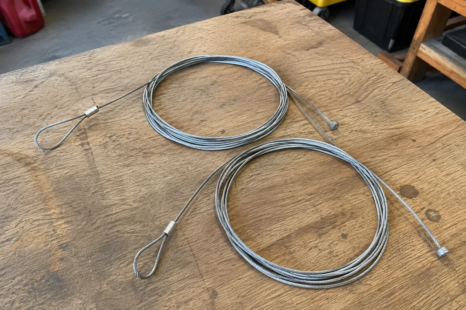 Two coiled steel cables with loop and stop ends on a workbench. — Garage Door Cable Replacement, Markham