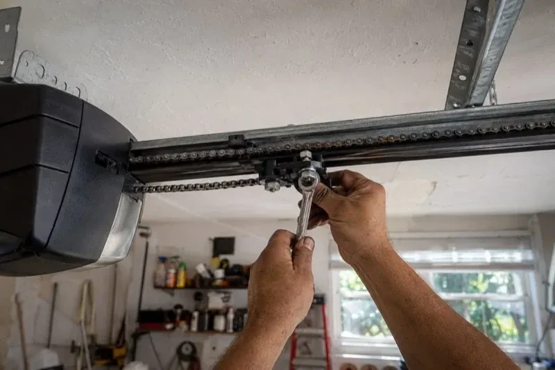 Hands holding a wrench against an opener trolley beneath a chain rail — Chain-Drive Opener Repair, Markham